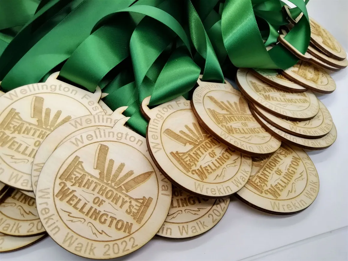 Stack of laser-engraved wood medals for Wrekin Walk 2022 Anthony of Wellington with green satin ribbon