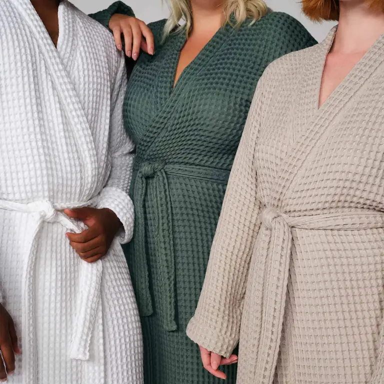 Three waffle-knit resort robes in white, sage green, and oat being modeled with tie waist