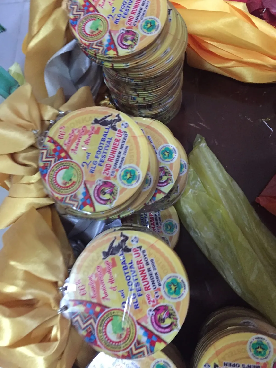 Stack of full-color sublimation printed medals for RLG Football Festival 2nd Runner Up with gold satin ribbon, logos and mascots
