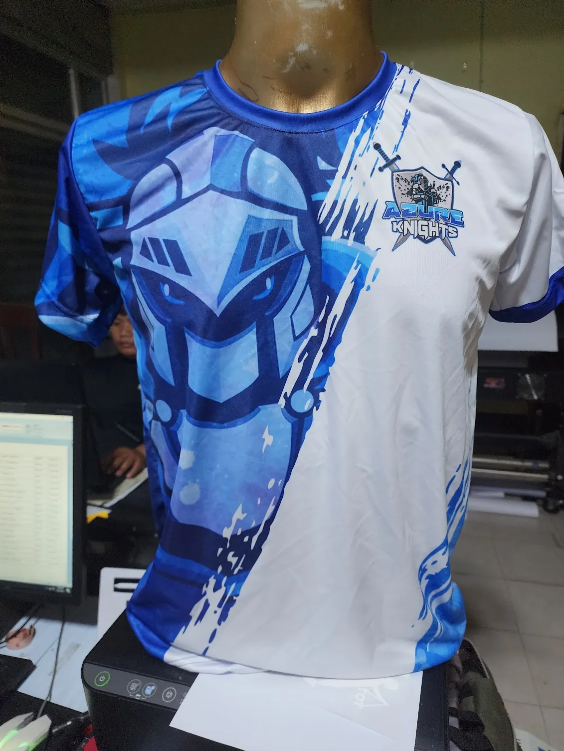 Blau weißes eSports Trikot mit ganzflächigem Sublimationsdruck auf einer Schaufensterpuppe mit Ritterhelm Motiv und Wappen des Teams Azure Knights.